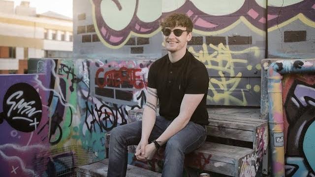 Picture of Ryan McMullan smiling sitting on a graffitied rooftop